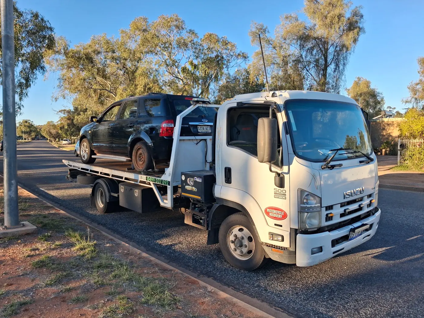A dark hatchback strapped on A.R Towing's tilt tray on an Alice Springs street