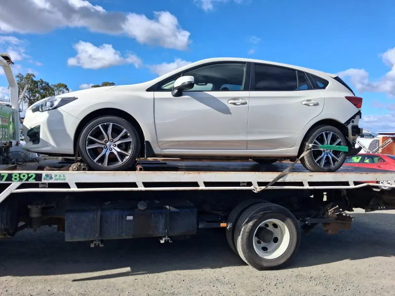 A white Subaru Impreza with rear damage strapped on the tilt tray