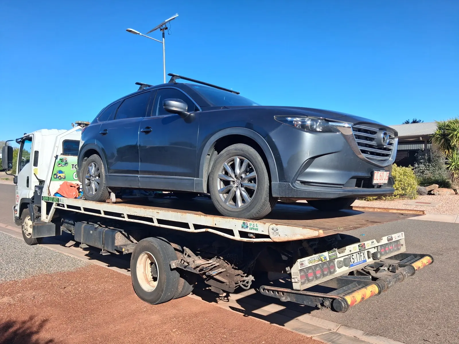 A grey Mazda CX-9 on the tilt tray beside a red-dirt kerb